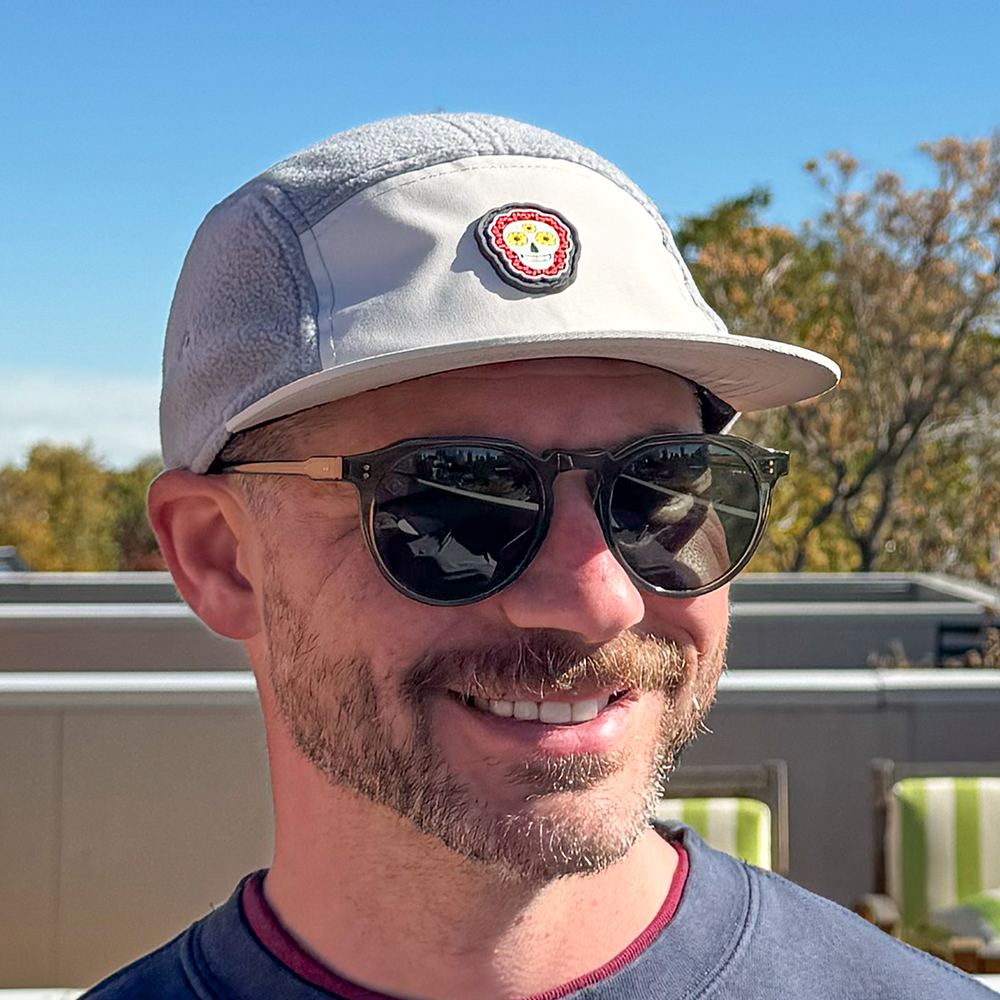 Front angled view of model wearing Skull Flower Fleece 5 Panel hat showing PVC skull flower patch