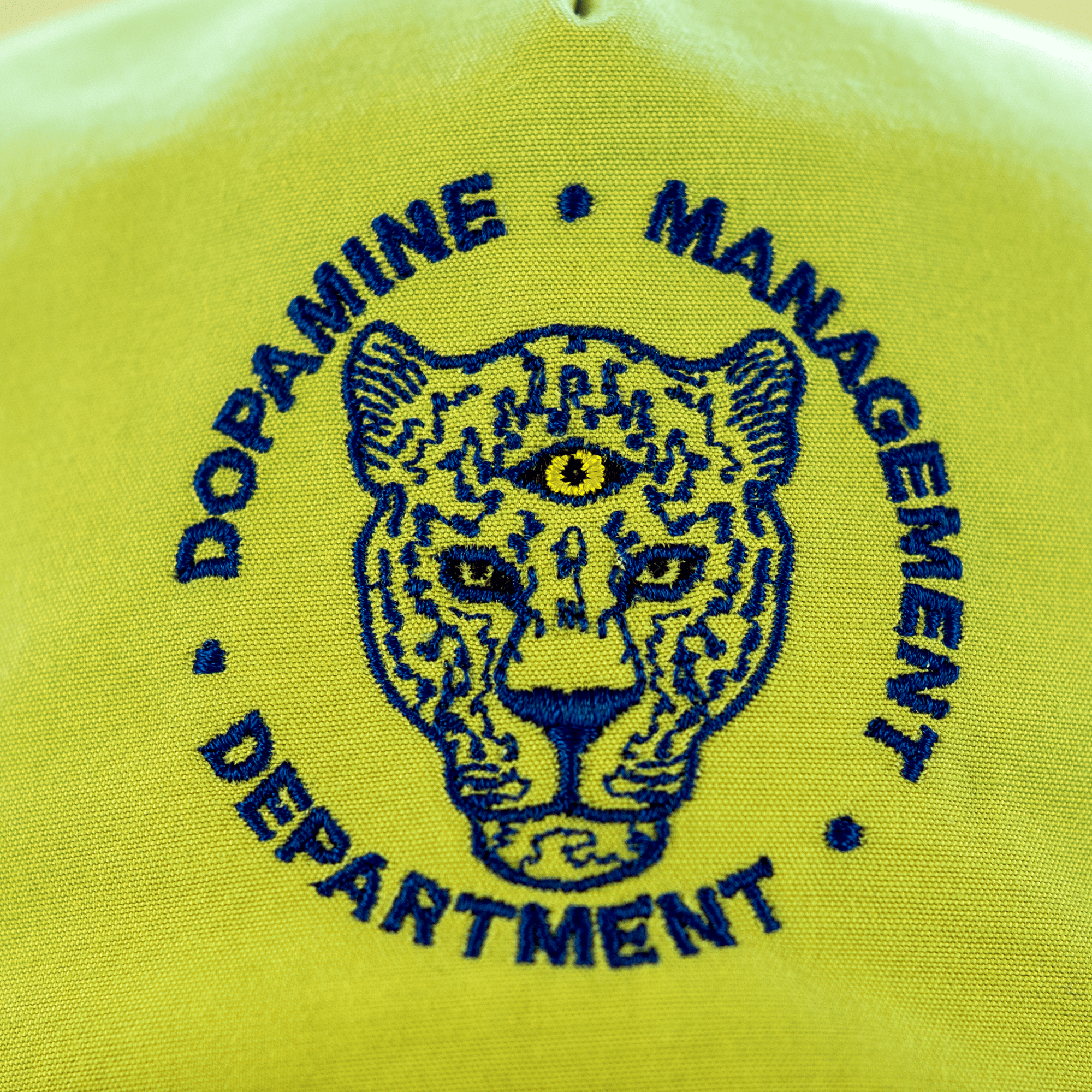 Embroidered logo on a pale green hat with a leopard design and text 'Dopamine Management Department'.