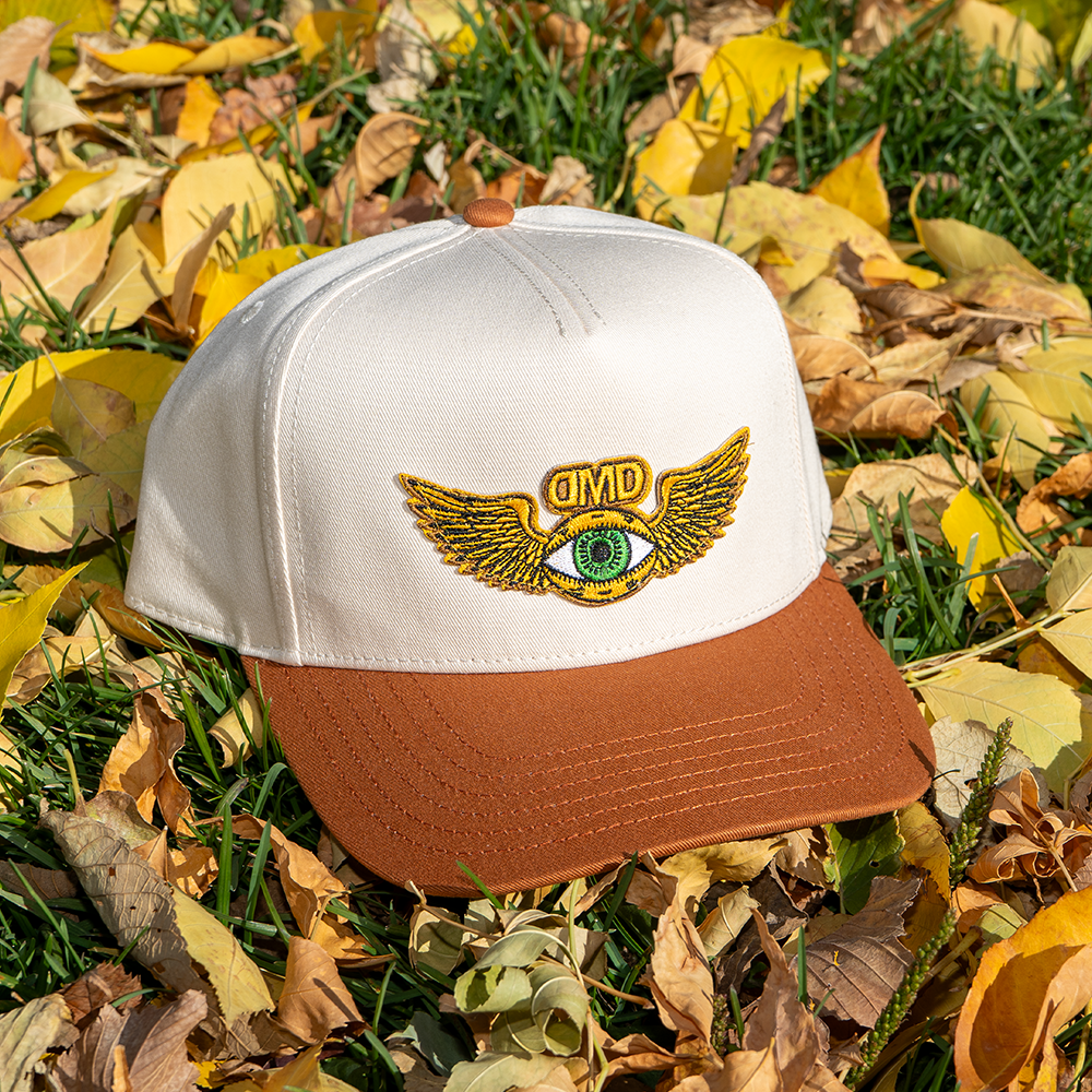 Flying Eye Two-Toned Hat resting on fall leaves – tan brim and cream crown