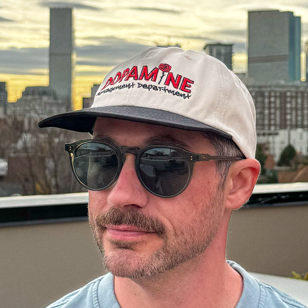 Side-angle lifestyle shot of the Rose Logo Hat worn with sunglasses.