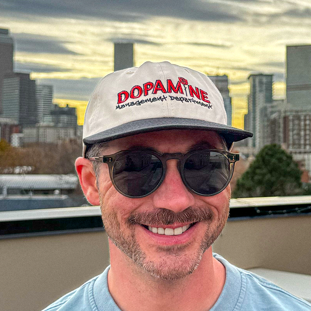Lifestyle photo of person smiling while wearing the Rose Logo Hat against a city skyline.