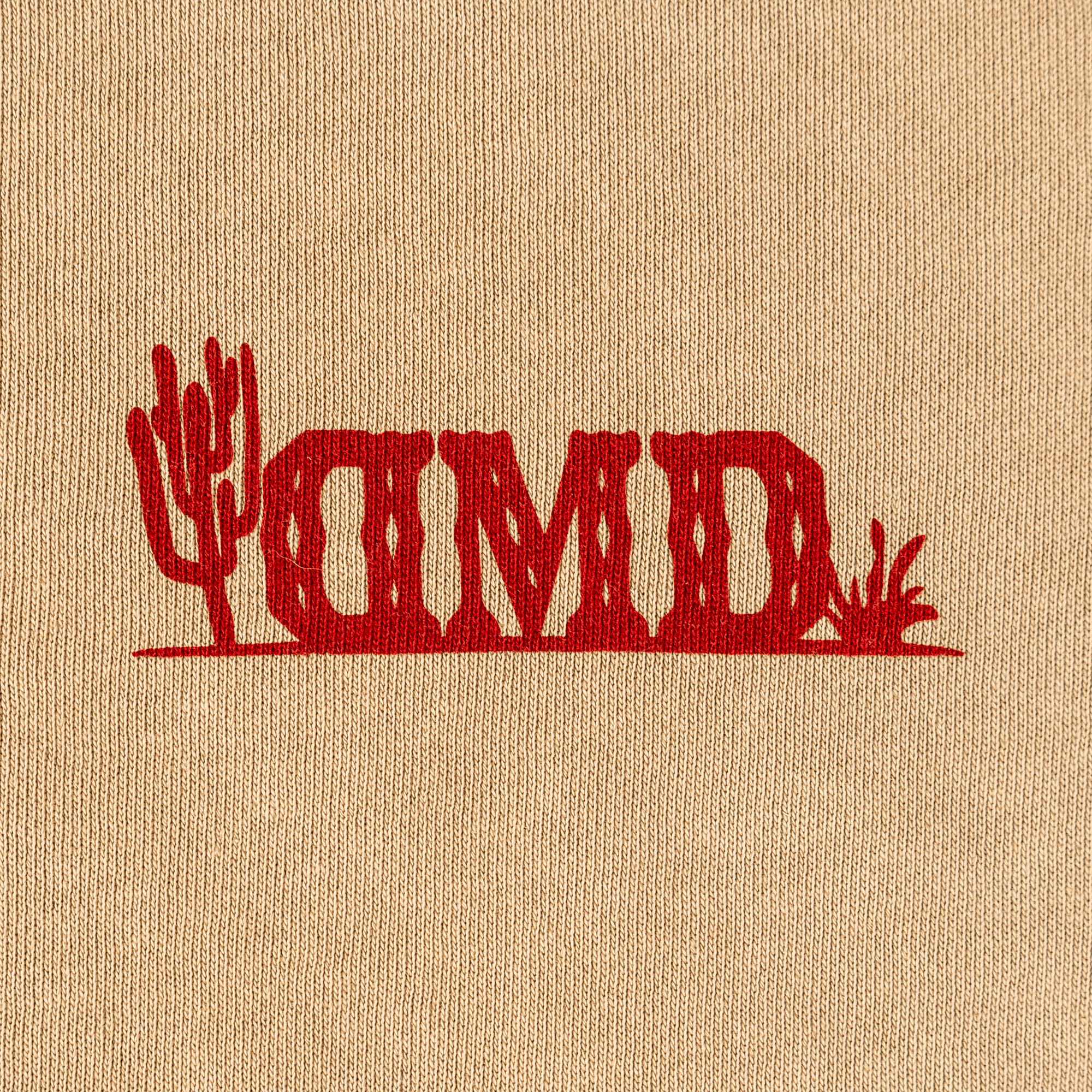 Detail shot of red DMD chest logo with cactus graphic on tan sweatshirt