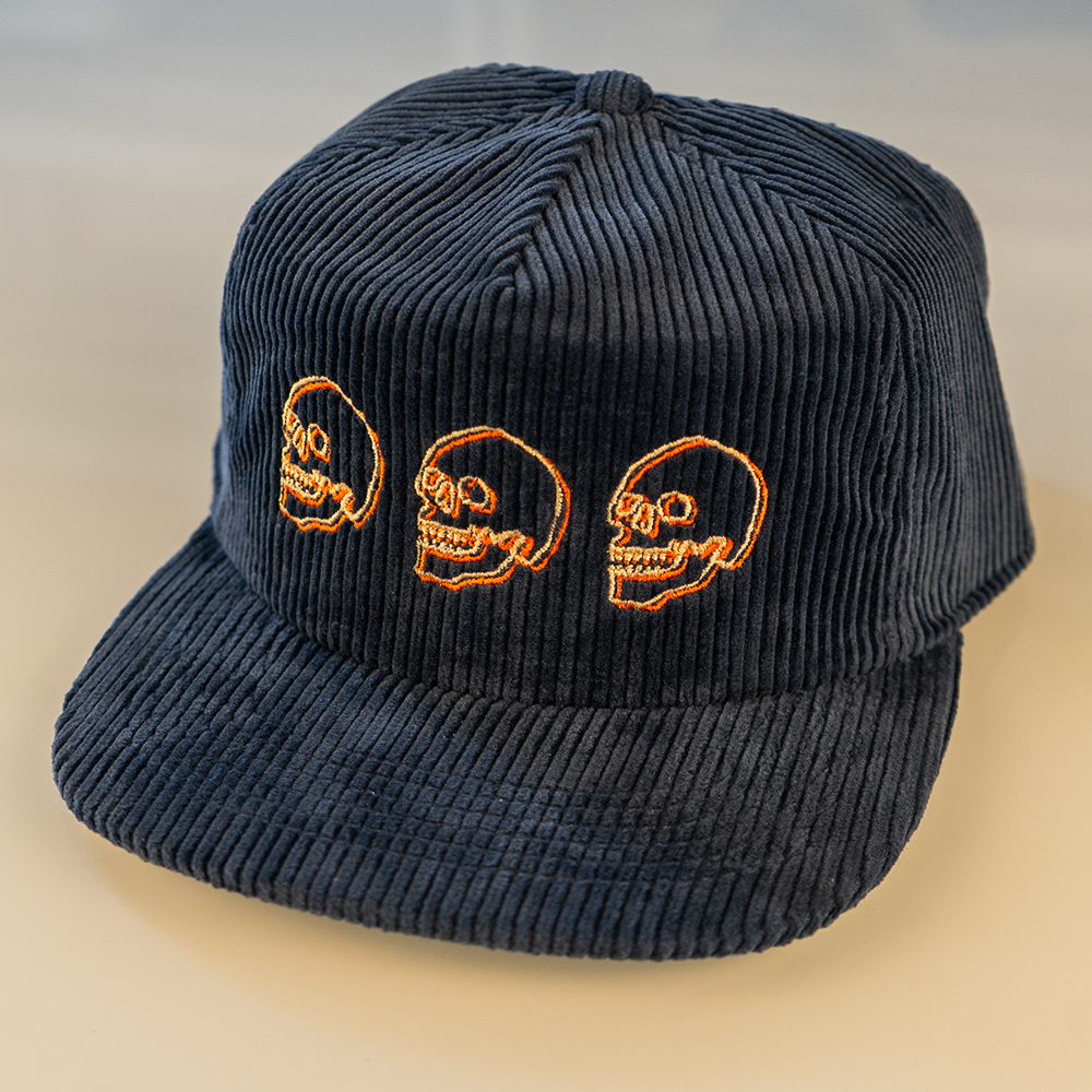 Side angle navy blue cotton corduroy cap with cream and orange skull embroidery.
