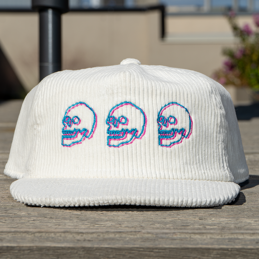 White corduroy cap with embroidered skulls on a wooden surface