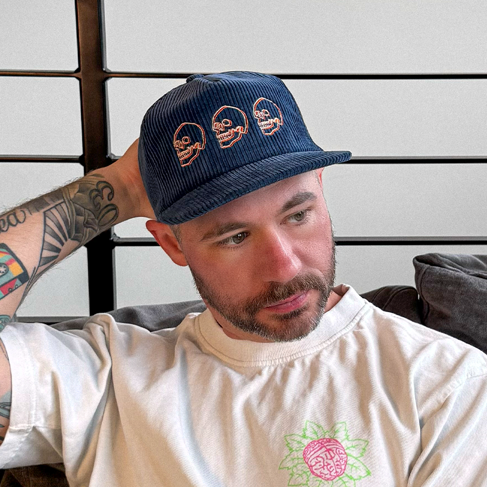 Man wearing a blue cotton corduroy cap with skull design embroidery.