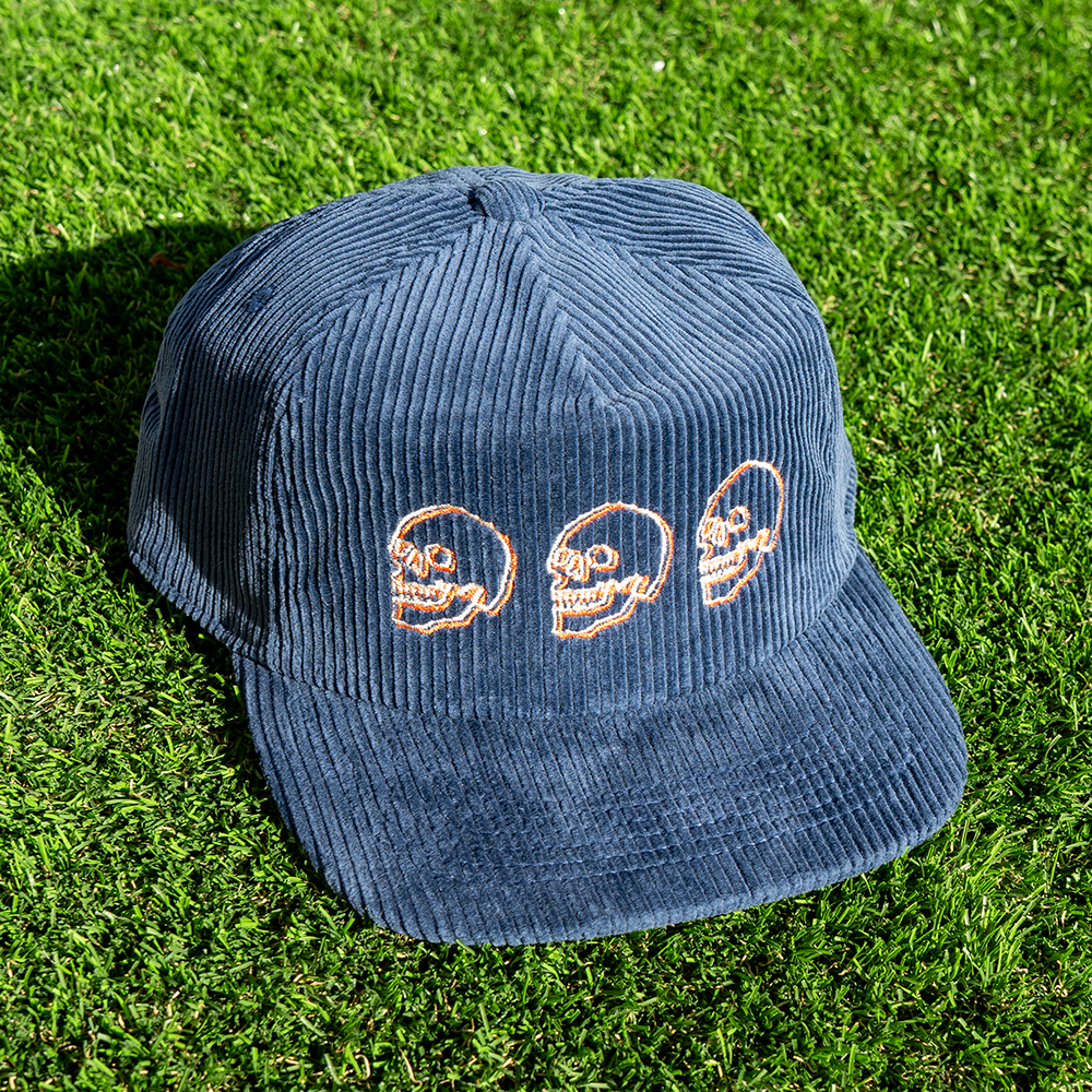 Navy blue corduroy cap with cream and orange embroidered skulls on grass