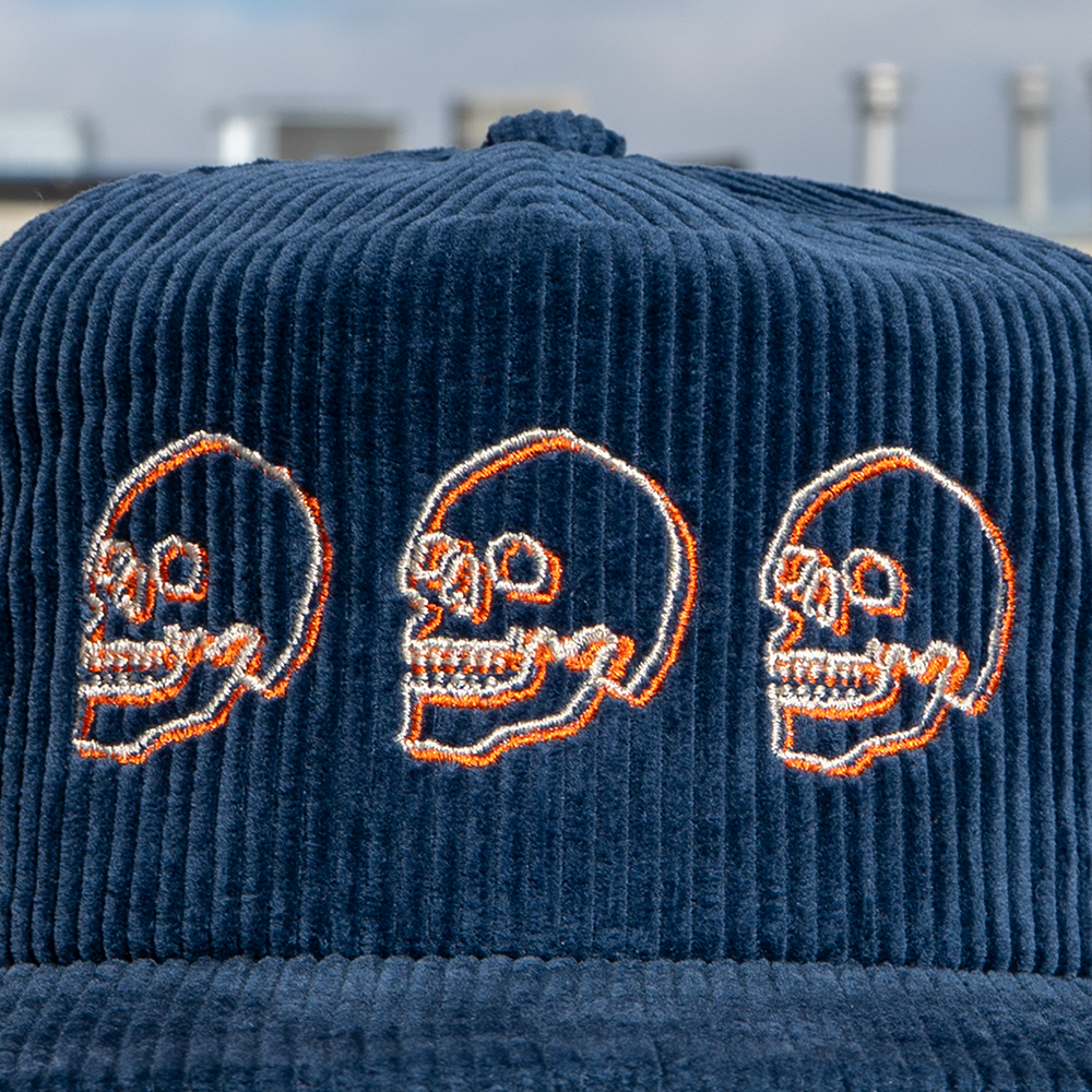 Navy blue corduroy cap with cream and orange embroidered skulls close up