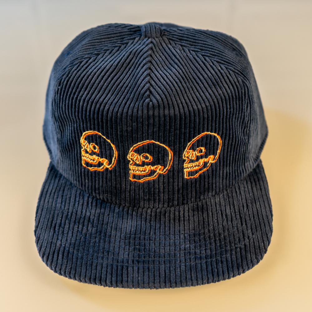 Navy blue cotton corduroy cap from above. Cream and orange skull embroidery. 