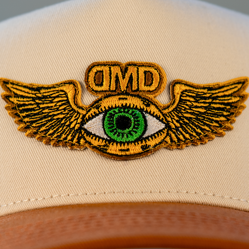 Close-up of Flying Eye embroidery on DMD hat – gold wings and green eye