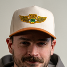 Close-up of model smiling in DMD Flying Eye Two-Toned Hat featuring gold winged eye embroidery