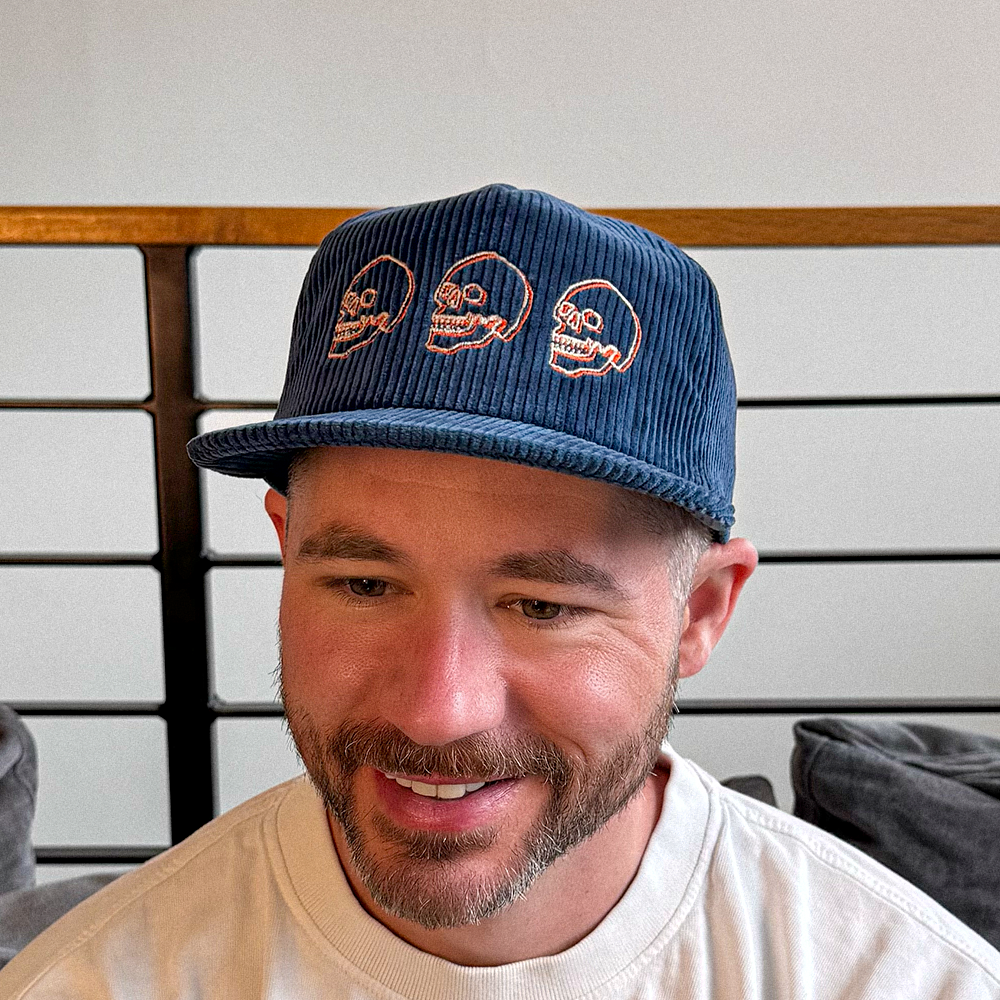 Man smiling wearing a blue cotton corduroy cap with skull designs 
