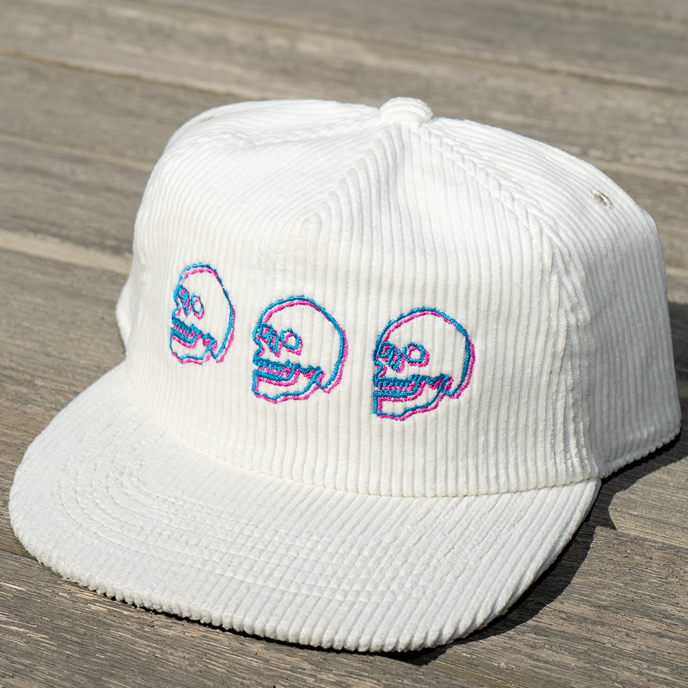 White corduroy cap with embroidered skulls on a wooden surface