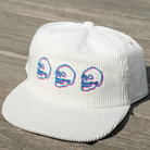 White corduroy cap with embroidered skulls on a wooden surface