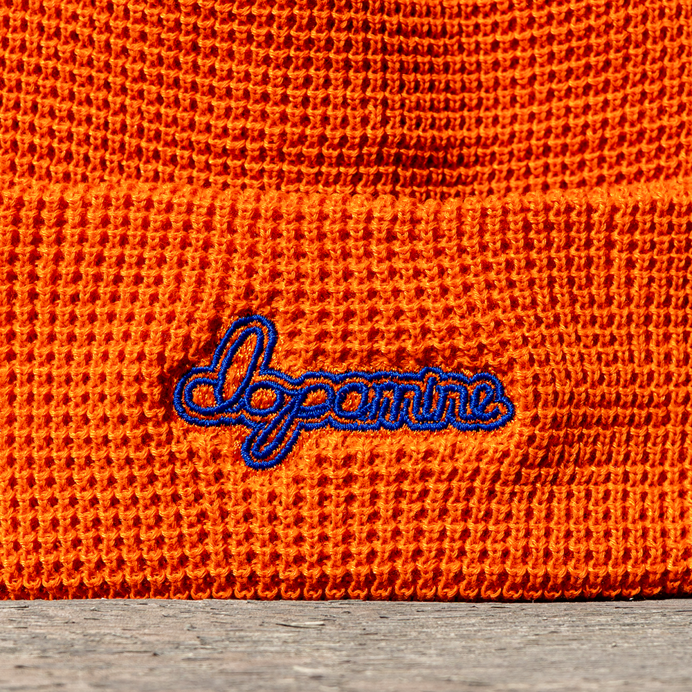 Close-up of an orange knitted fabric with 'Dopamine' embroidered in blue