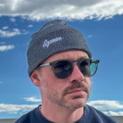 Model wearing grey & black Script Beanie against blue sky