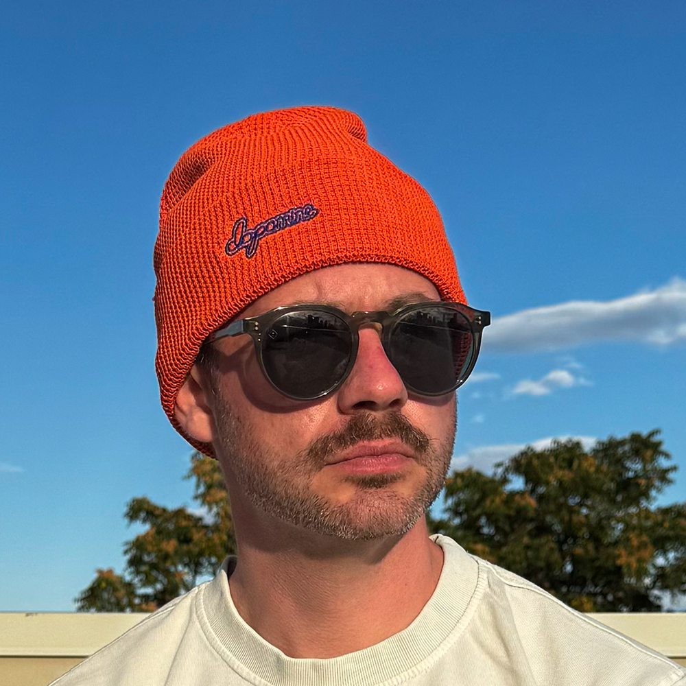 Model wearing orange Script Beanie against blue sky