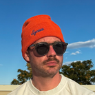 Model wearing orange Script Beanie against blue sky