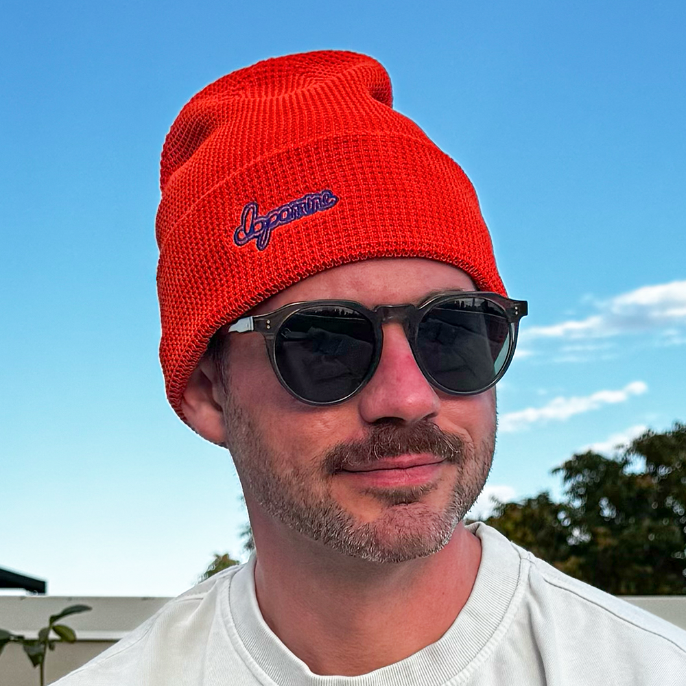 Model wearing orange Script Beanie against blue sky
