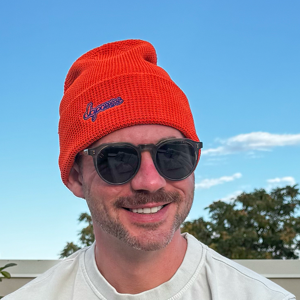 Model wearing orange Script Beanie against blue sky