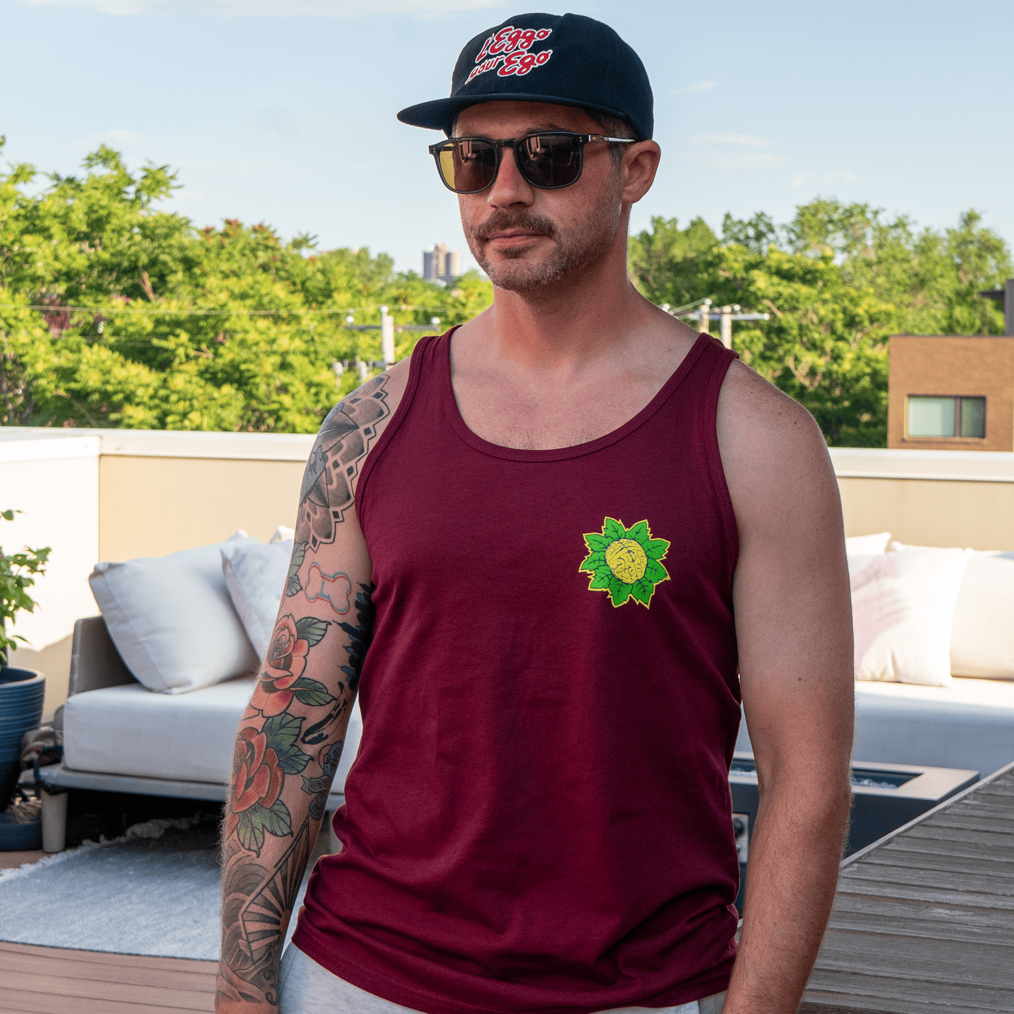 Tattooed model in maroon unisex tank top with green and yellow brain-flower graphic