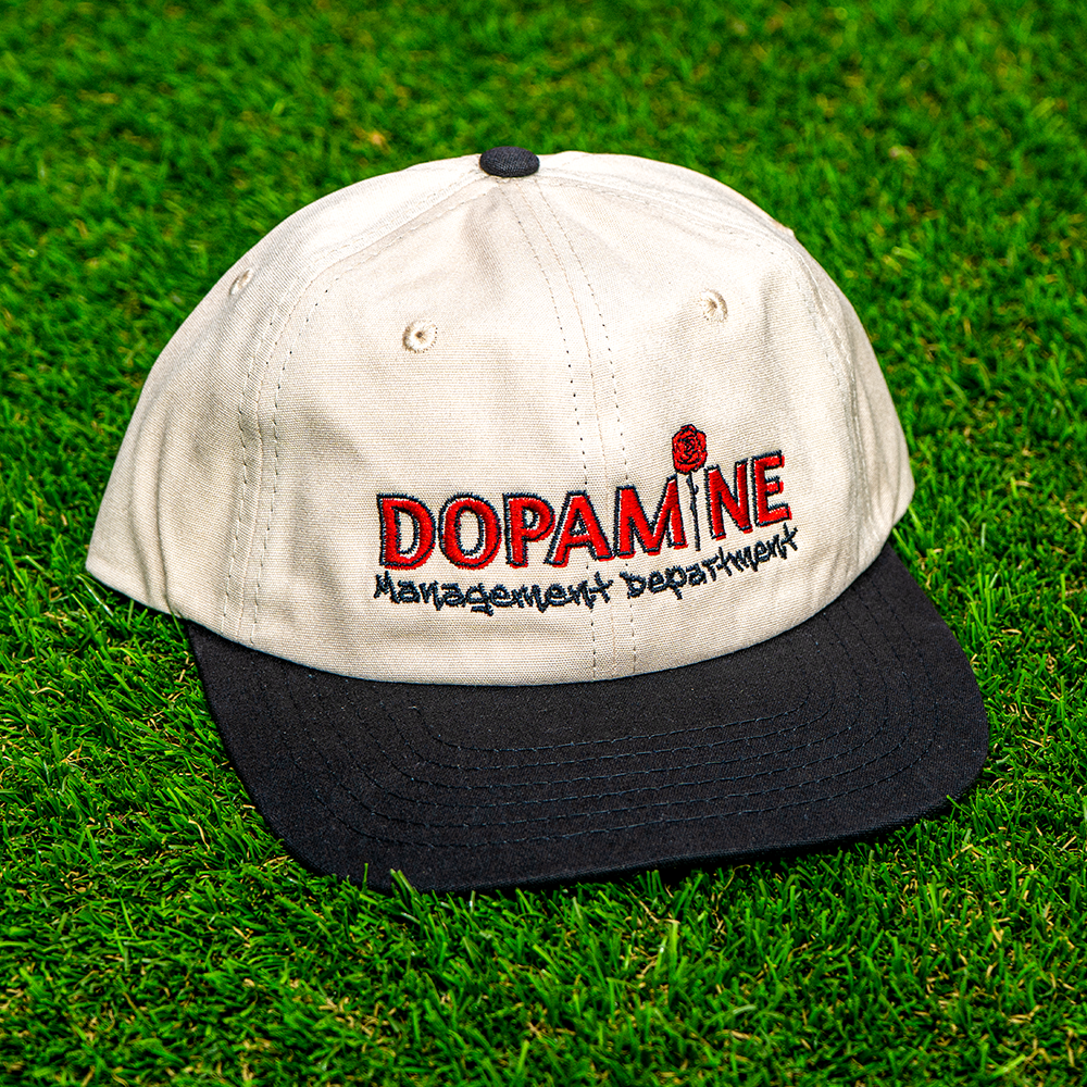 Rose Logo Hat placed on grass highlighting two-tone design and red rose embroidery.