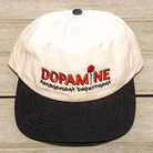 Front view of the Rose Logo Hat showing cream crown and black brim on table surface.