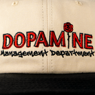 Close-up embroidery detail of the Dopamine Management Department rose logo on cream canvas.