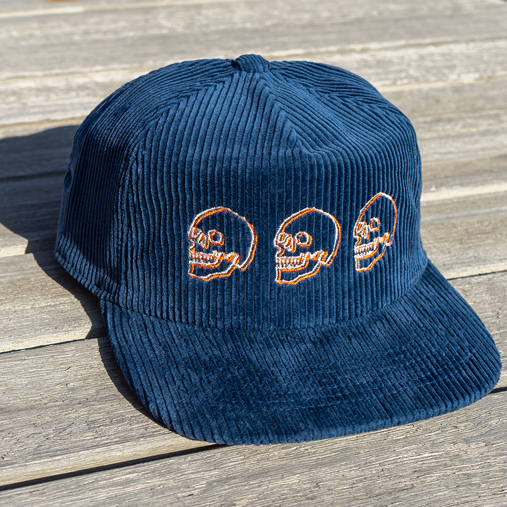 Navy blue corduroy cap with cream and  orange embroidered skulls angled