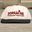 Front view of the Rose Logo Hat showing cream crown and black brim on table surface.